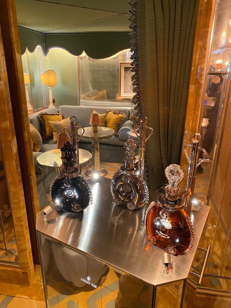 Détail du chariot Louis XIII de Rémy Martin : carafes en cristal sur plateau métal, salon feutré en arrière-plan