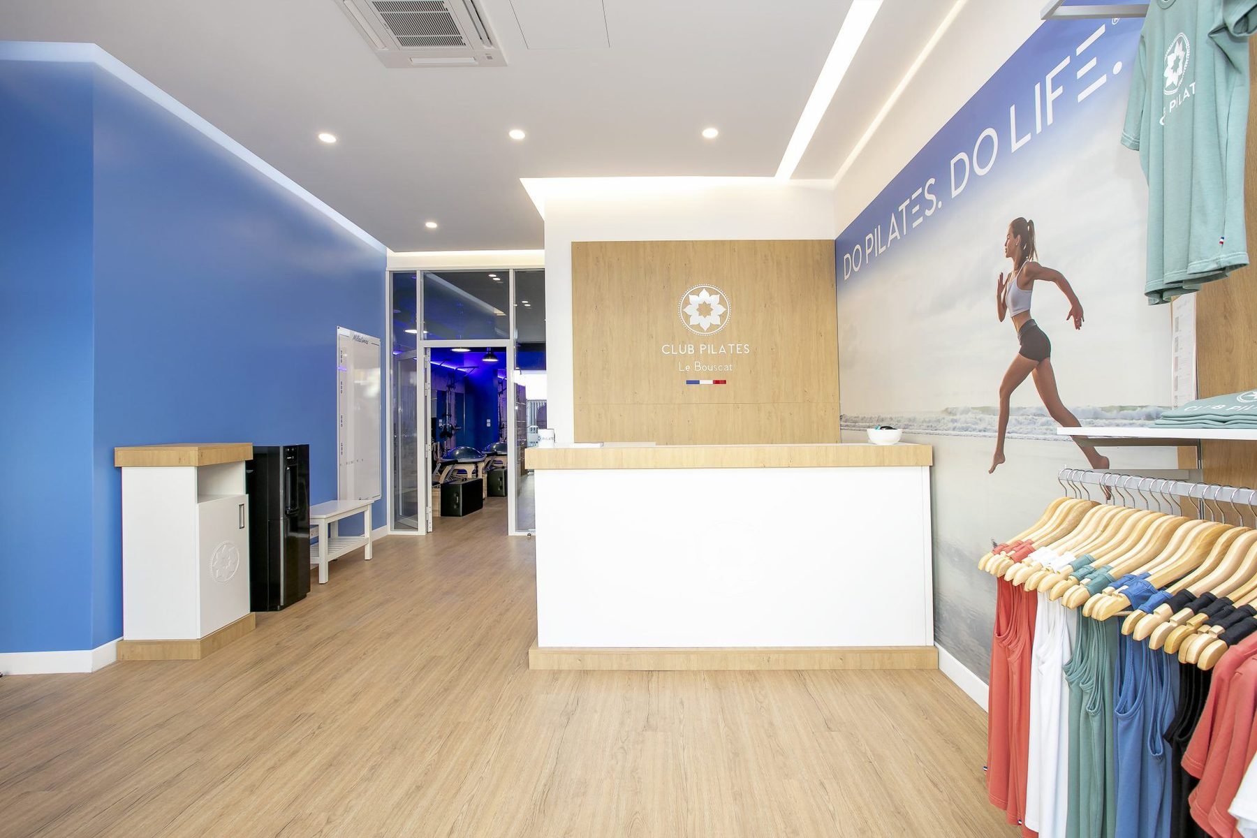 Comptoir d'accueil avec logo Club Pilates et présentoir de vêtements sur mur bleu