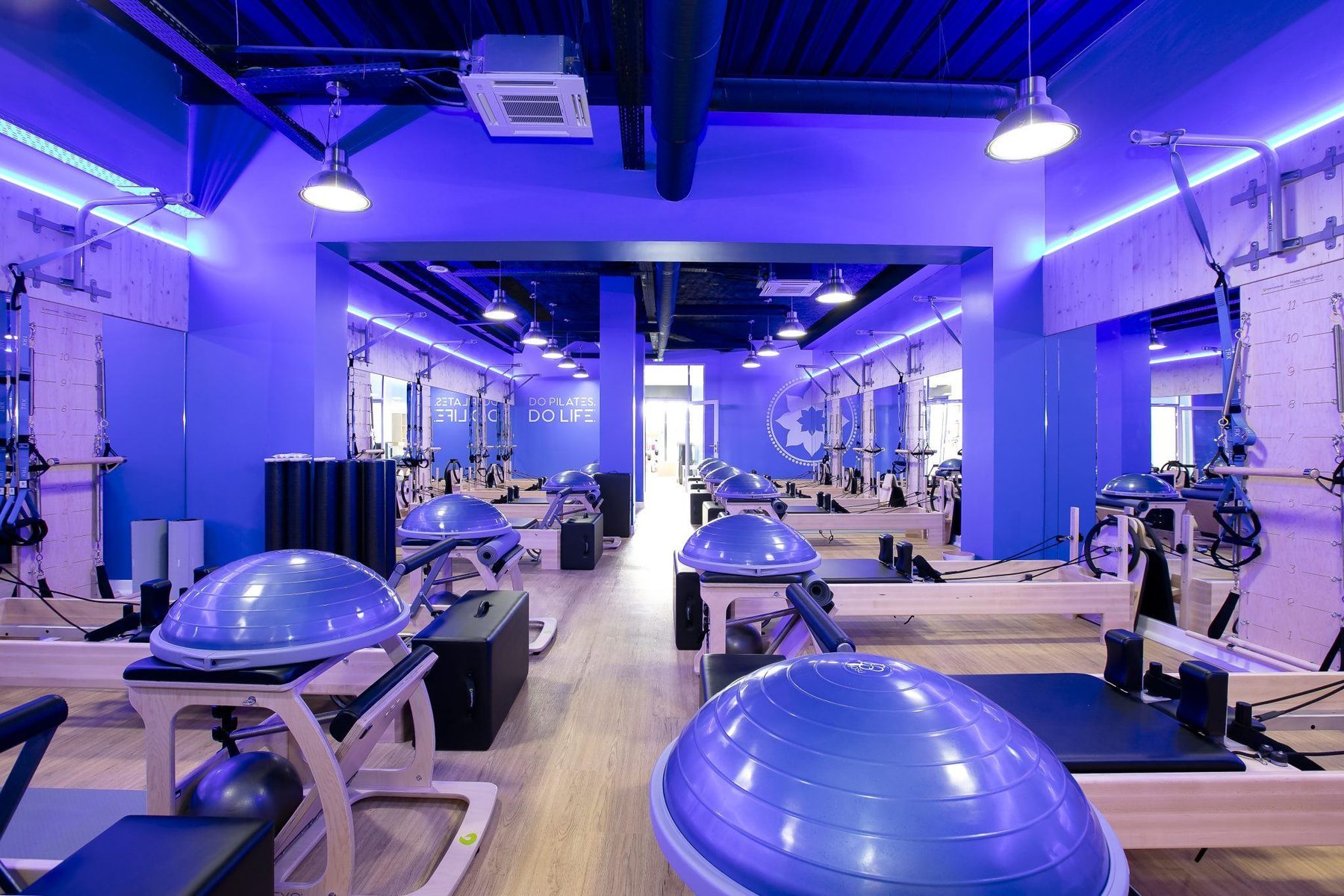 Salle d'entraînement du Club Pilates Le Bouscat : reformers alignés sous éclairage néon bleu et plafond noir industriel