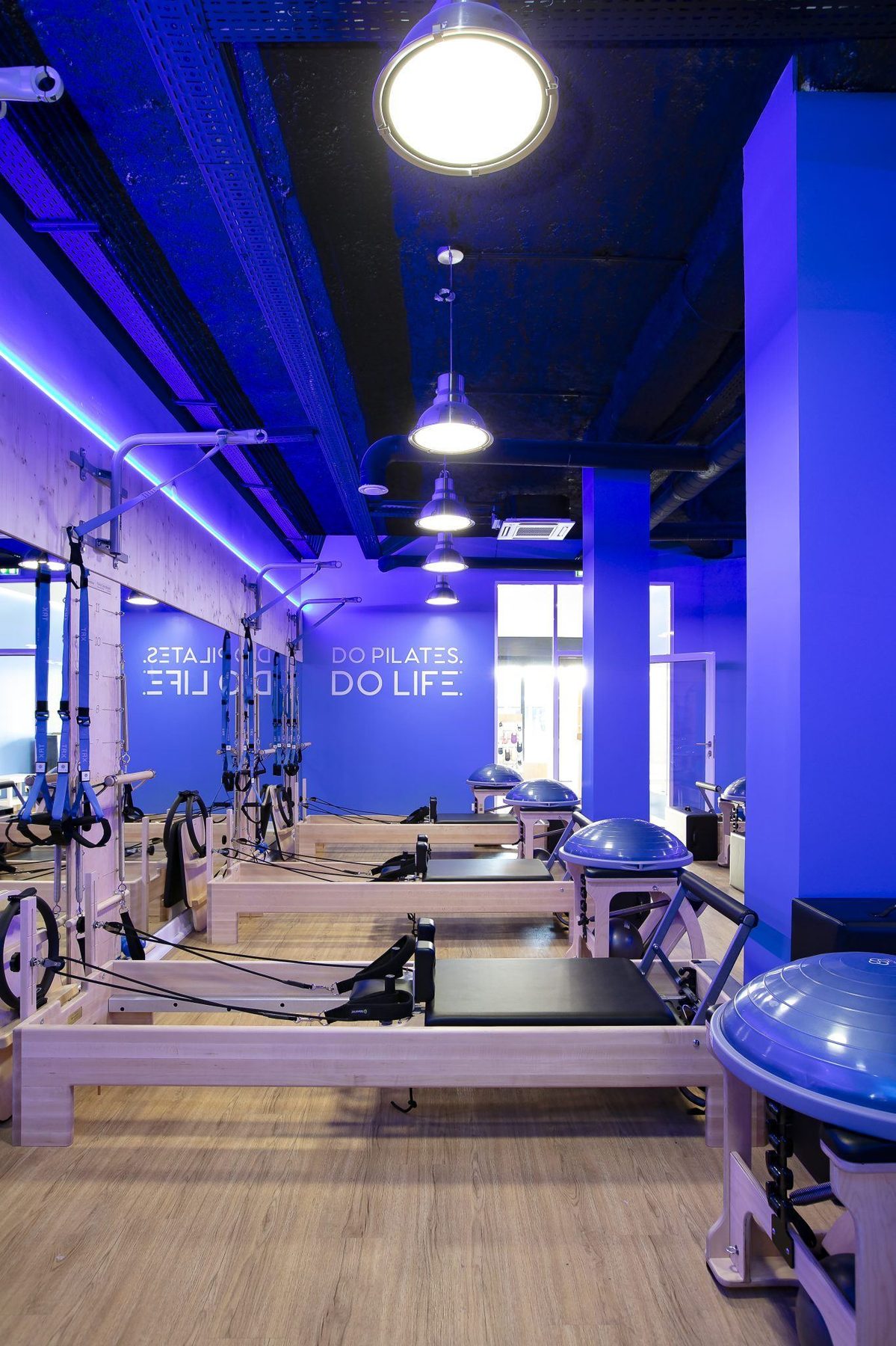 Perspective verticale sur les reformers alignés et la signature murale DO PILATES DO LIFE