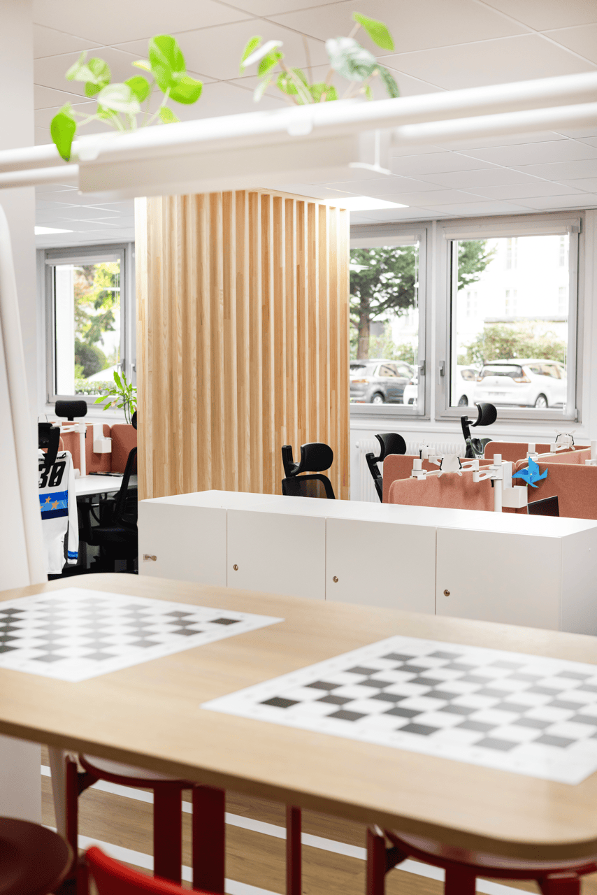 Espace de pause avec claustra en bois clair et tables motif damier