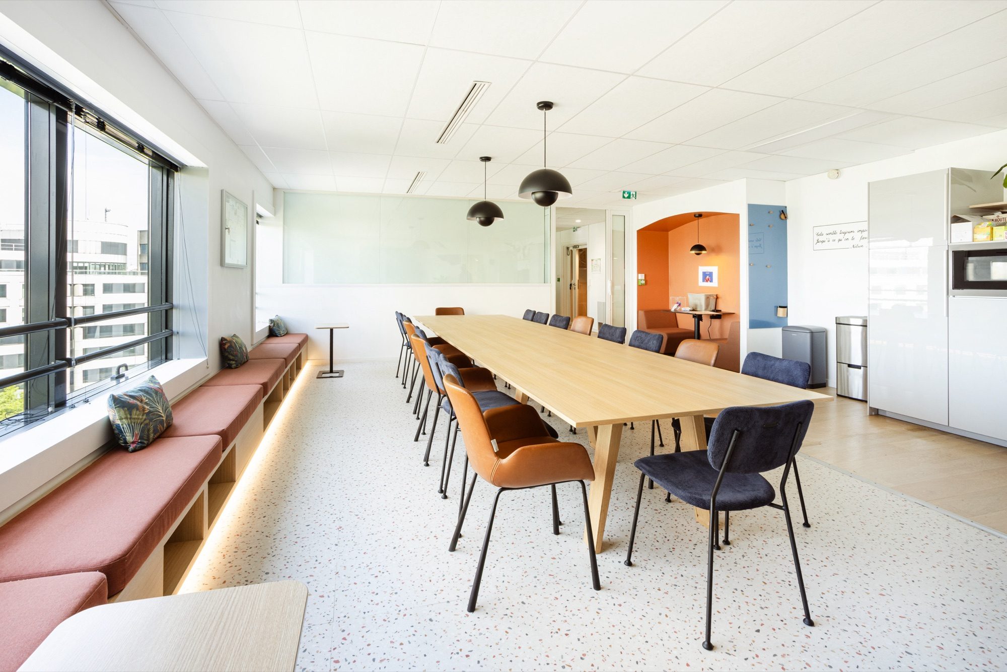 Salle conviviale avec banquette terracotta et kitchenette dans des bureaux pharmaceutiques