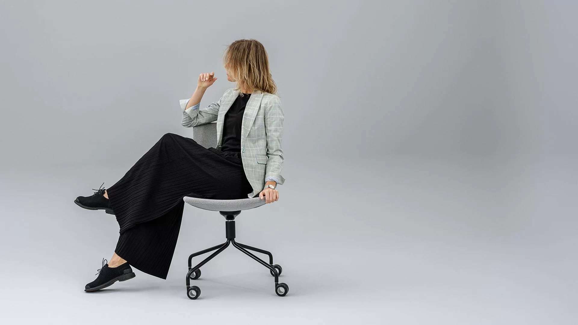 Femme assise sur une chaise de réunion en tissu gris, piétement étoile noir à roulettes