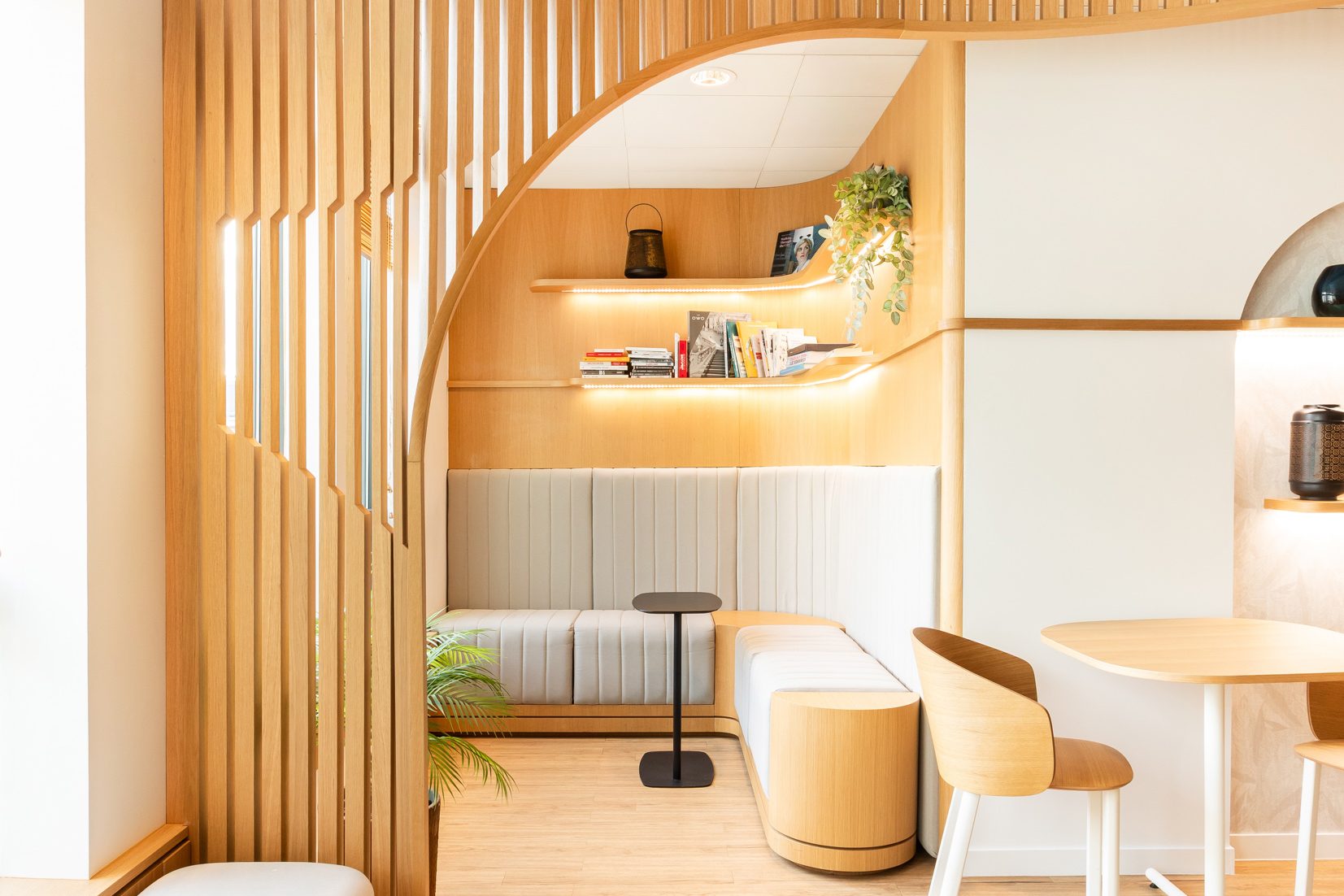 Petit espace détente au 25 BM aménagé par Isospace : claustra bois vertical, banquette capitonnée et étagères murales avec plantes