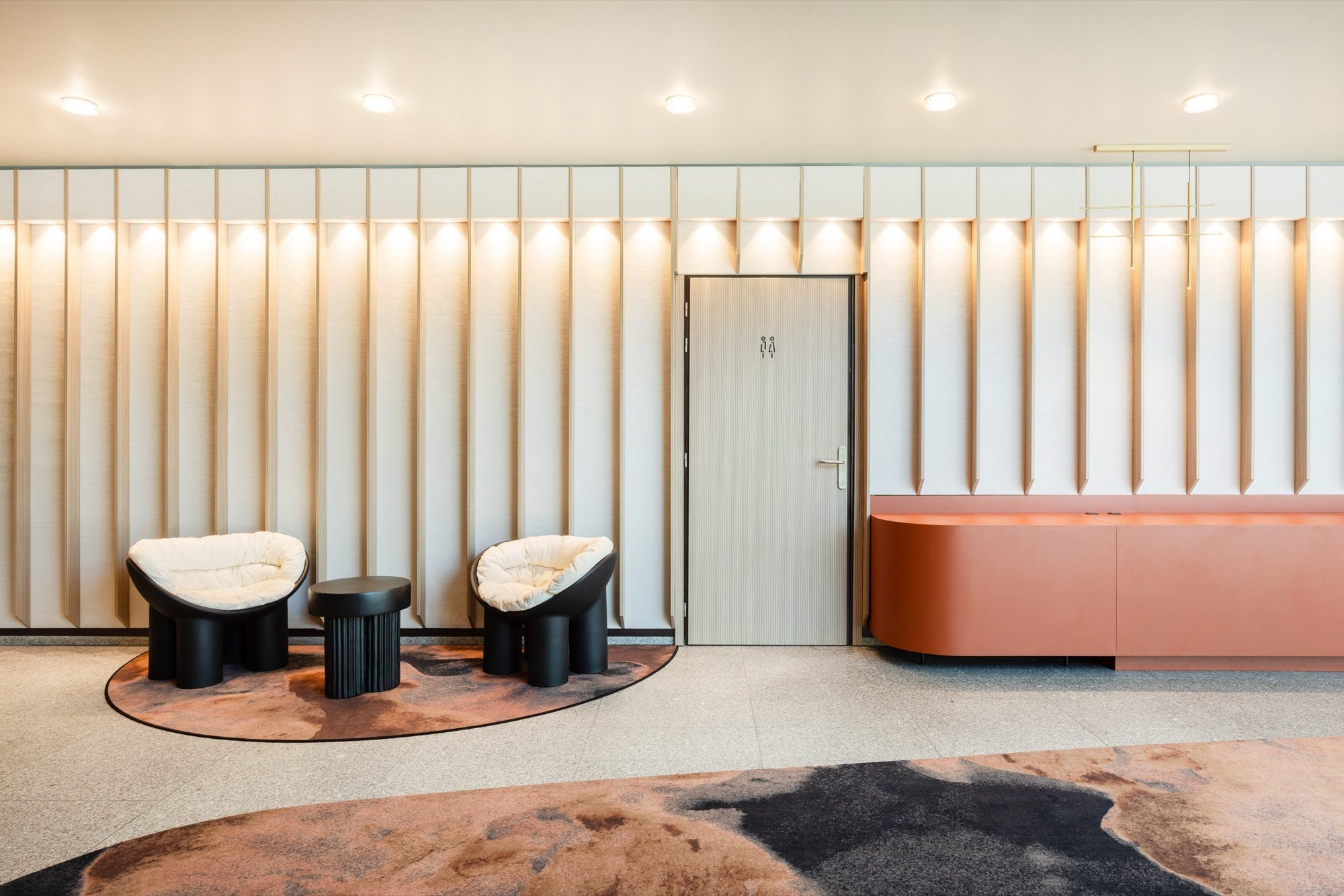 Coin d'attente avec fauteuils ronds, mur cannelé rétroéclairé et meuble bas orange