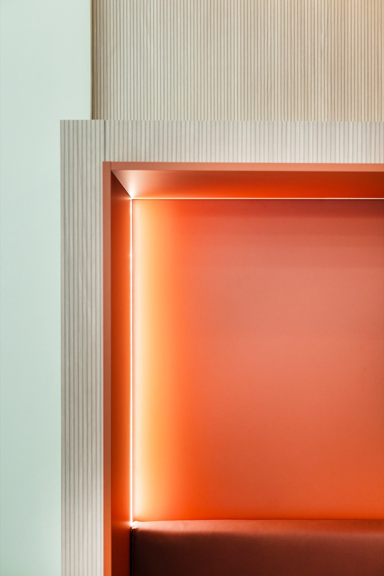 Détail d'une niche rétroéclairée orange encadrée de bois cannelé clair, sur fond vert d'eau