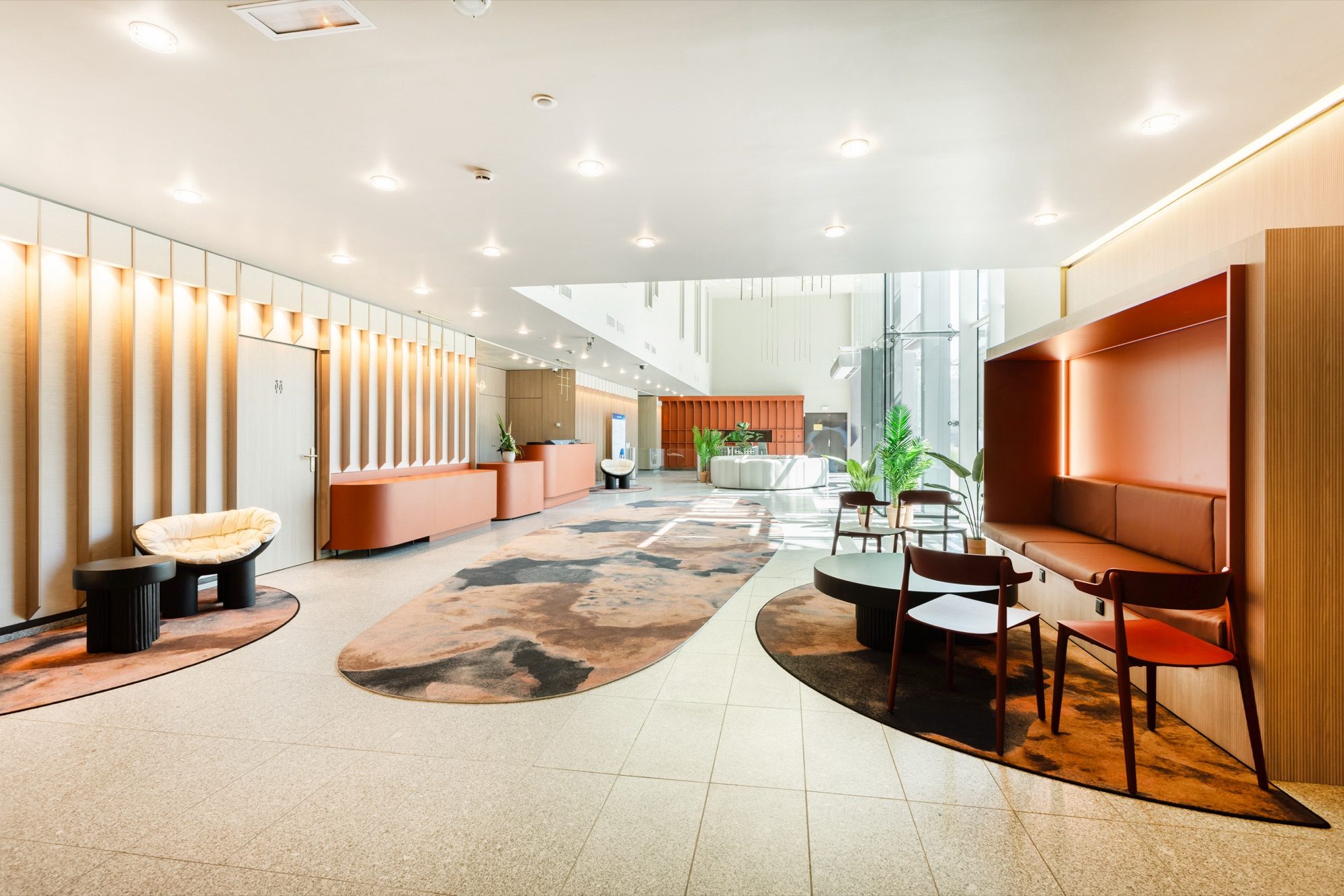 Coin d'accueil avec banquette orange sur mesure, fauteuils et tapis organique dans le hall du siège
