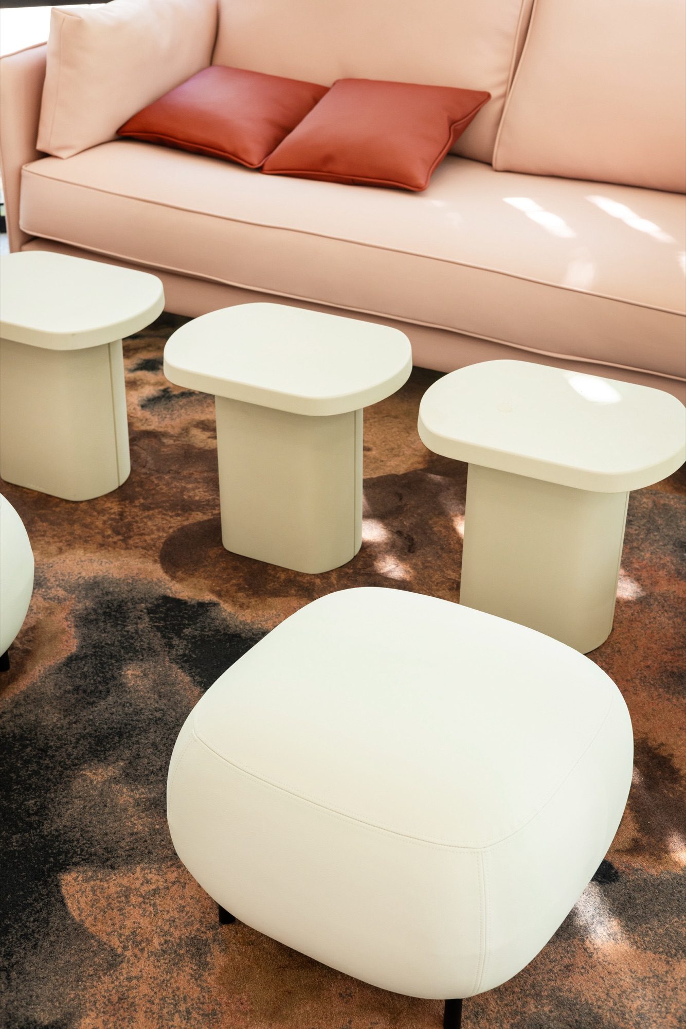 Salon détente : canapé cuir rose poudré, poufs et tables d'appoint vert pâle sur tapis organique