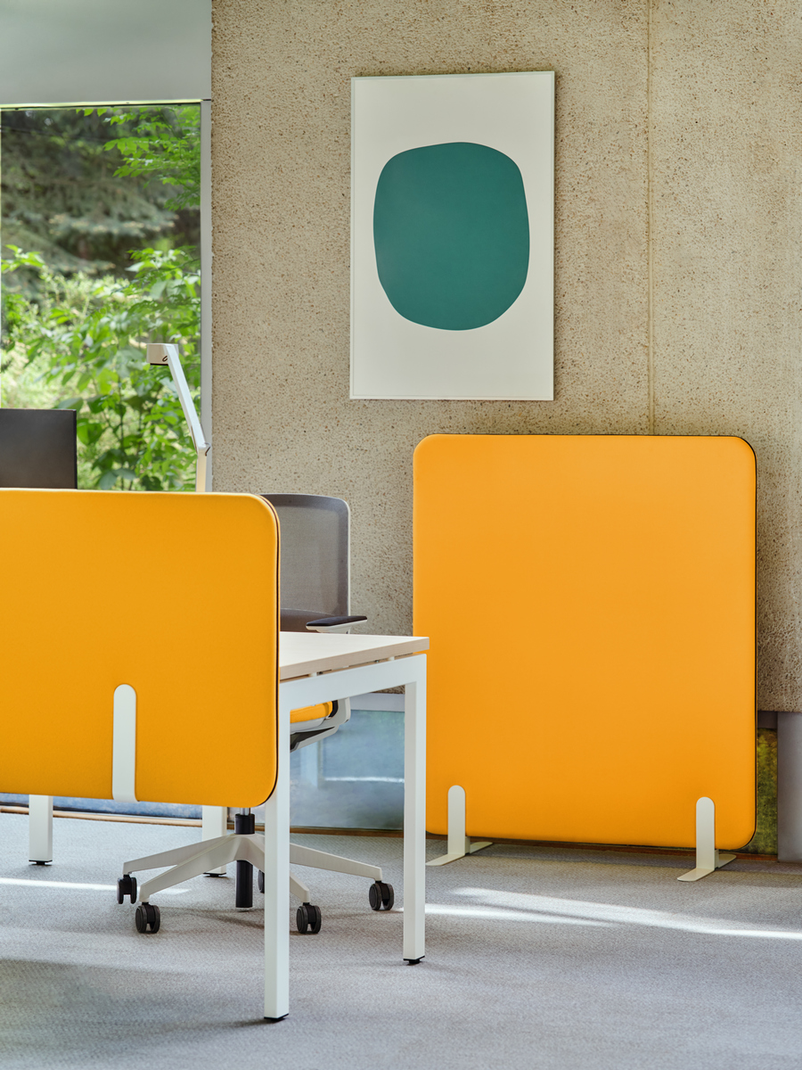 Panneau acoustique sur pied orange installé à côté d'un poste de travail en open space