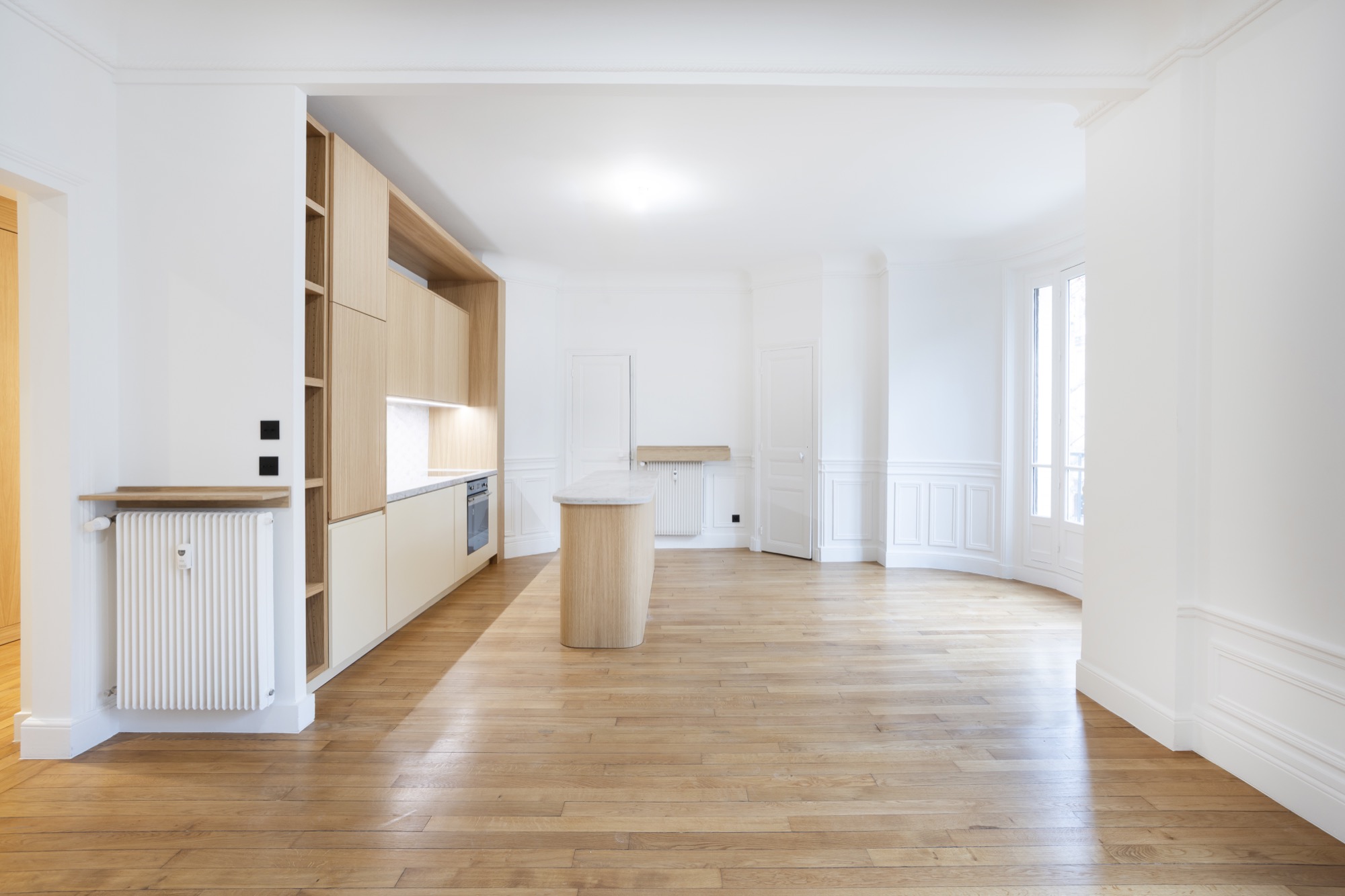 Séjour rénové d'un appartement haussmannien à Paris : parquet chêne, îlot de cuisine et moulures