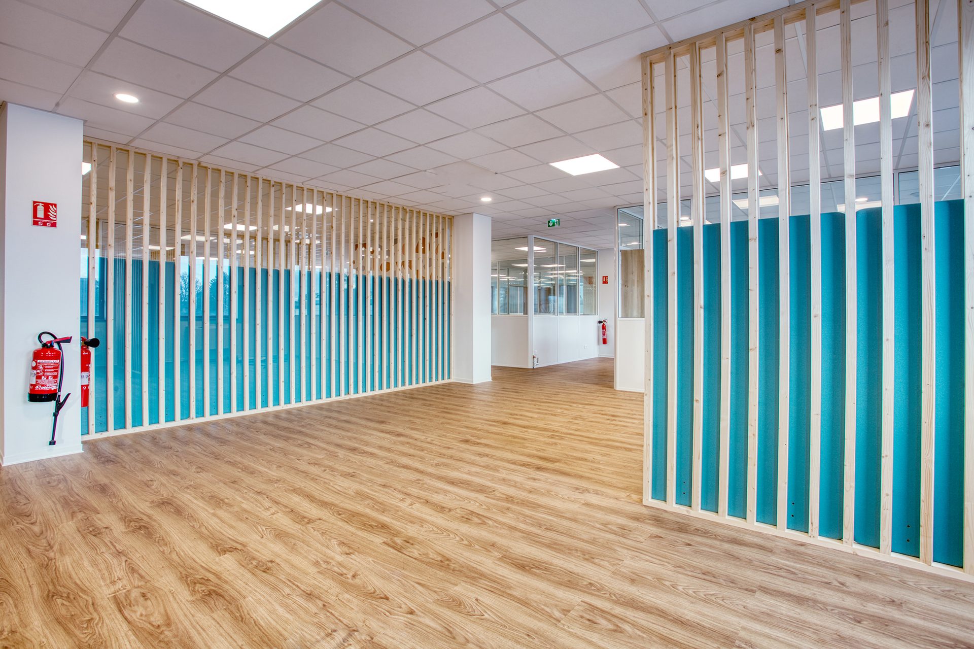 Couloir rythmé par des claustras en bois et des panneaux acoustiques turquoise, laboratoire aménagé en flex office par Isospace à Paris