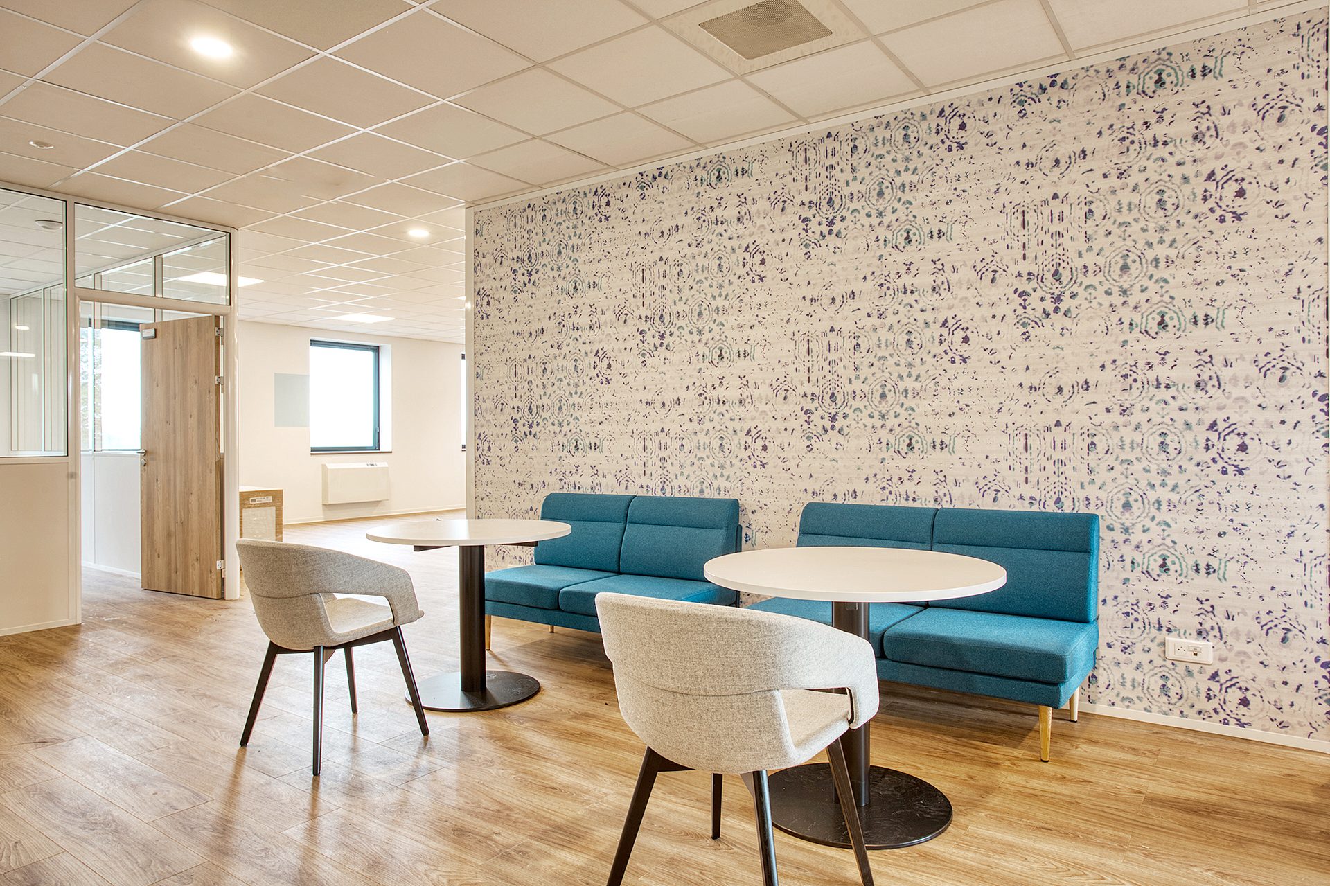 Espace détente avec banquette turquoise, fauteuils et papier peint fleuri, laboratoire aménagé par Isospace