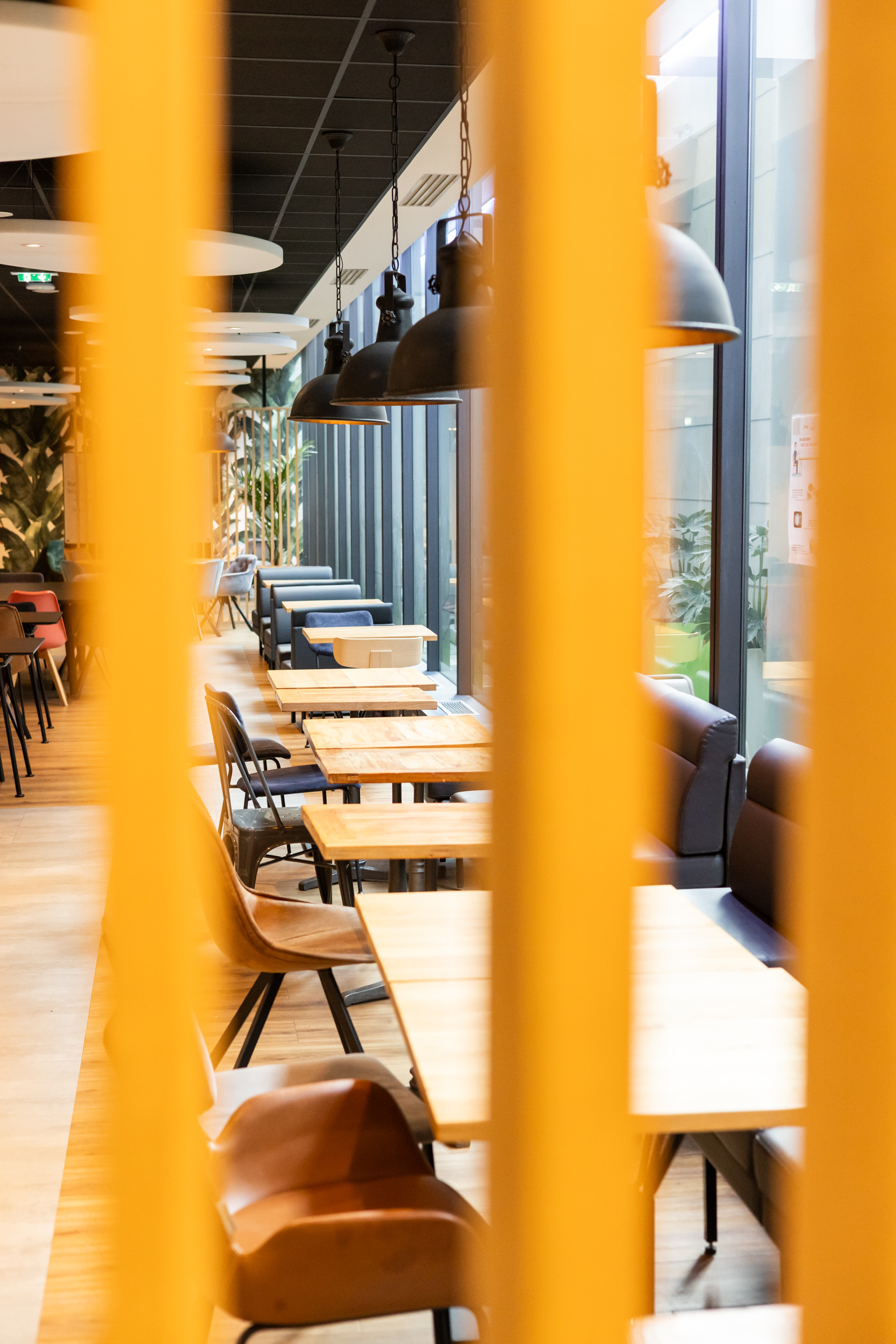 Coin repas de la cafétéria Free, tables bois et banquettes le long des baies