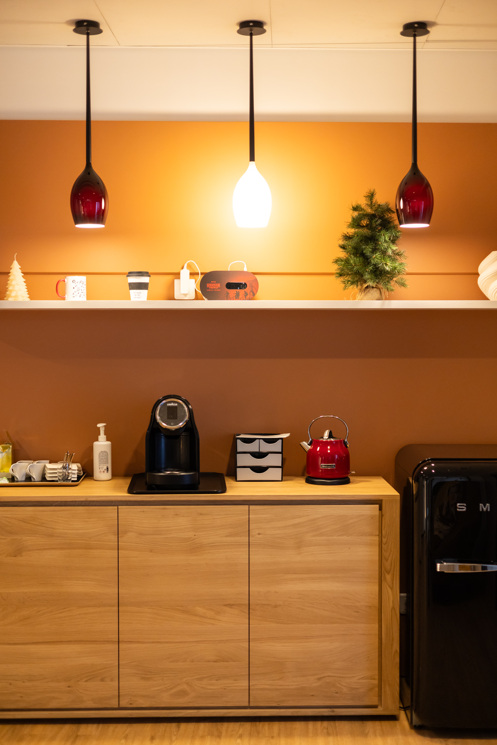 Coin café avec suspensions colorées, mur terracotta et rangements en chêne