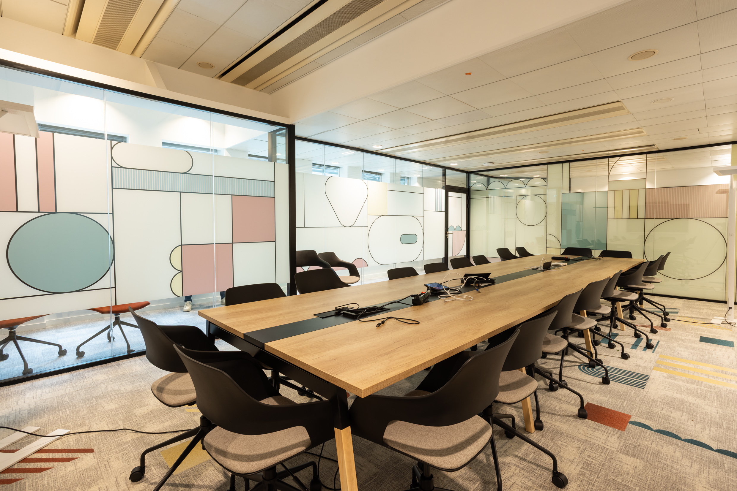 Grande salle de réunion aux cloisons vitrées habillées d'un décor graphique pastel