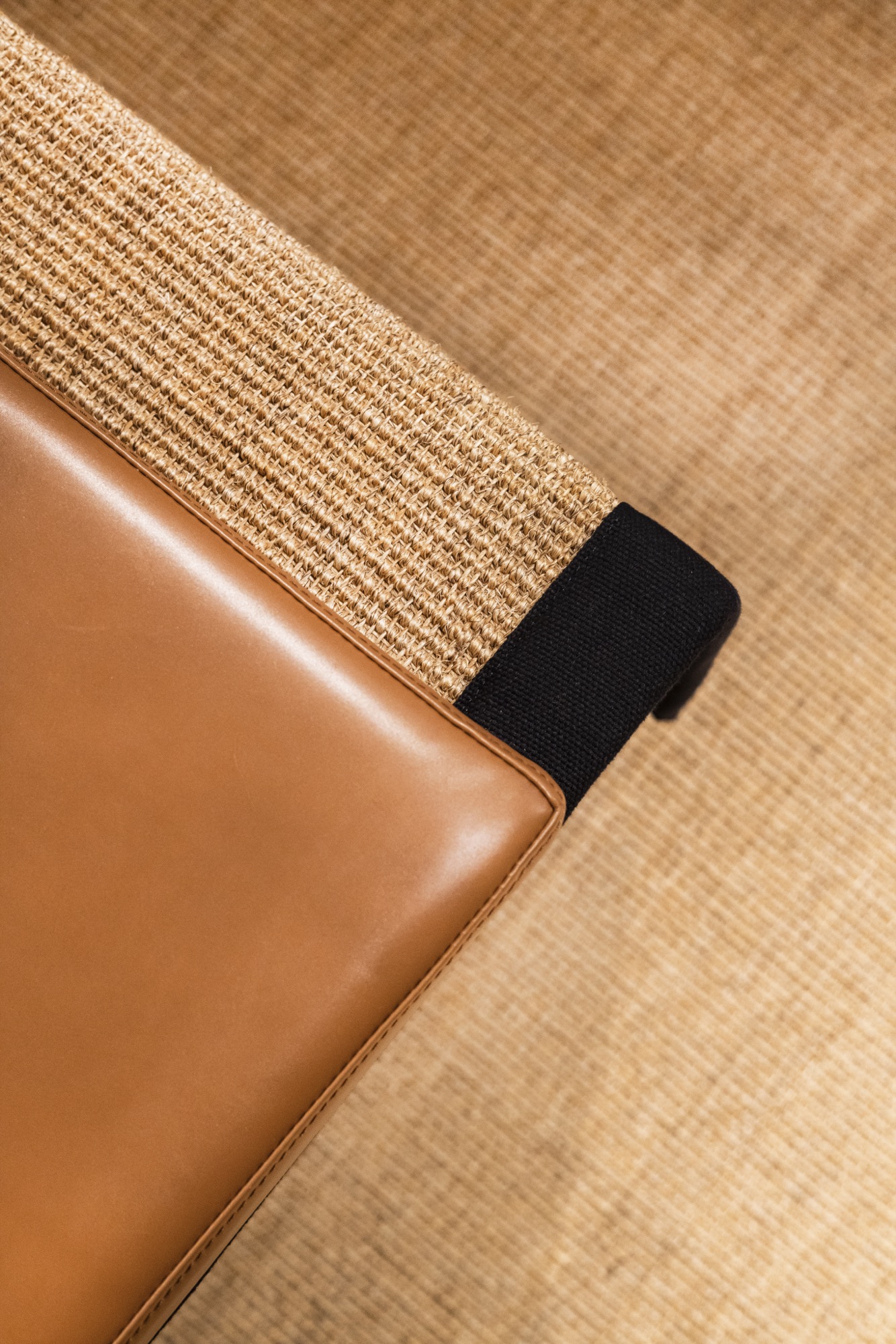 Détail du plateau en sisal bordé de toile noire et du banc en cuir cognac