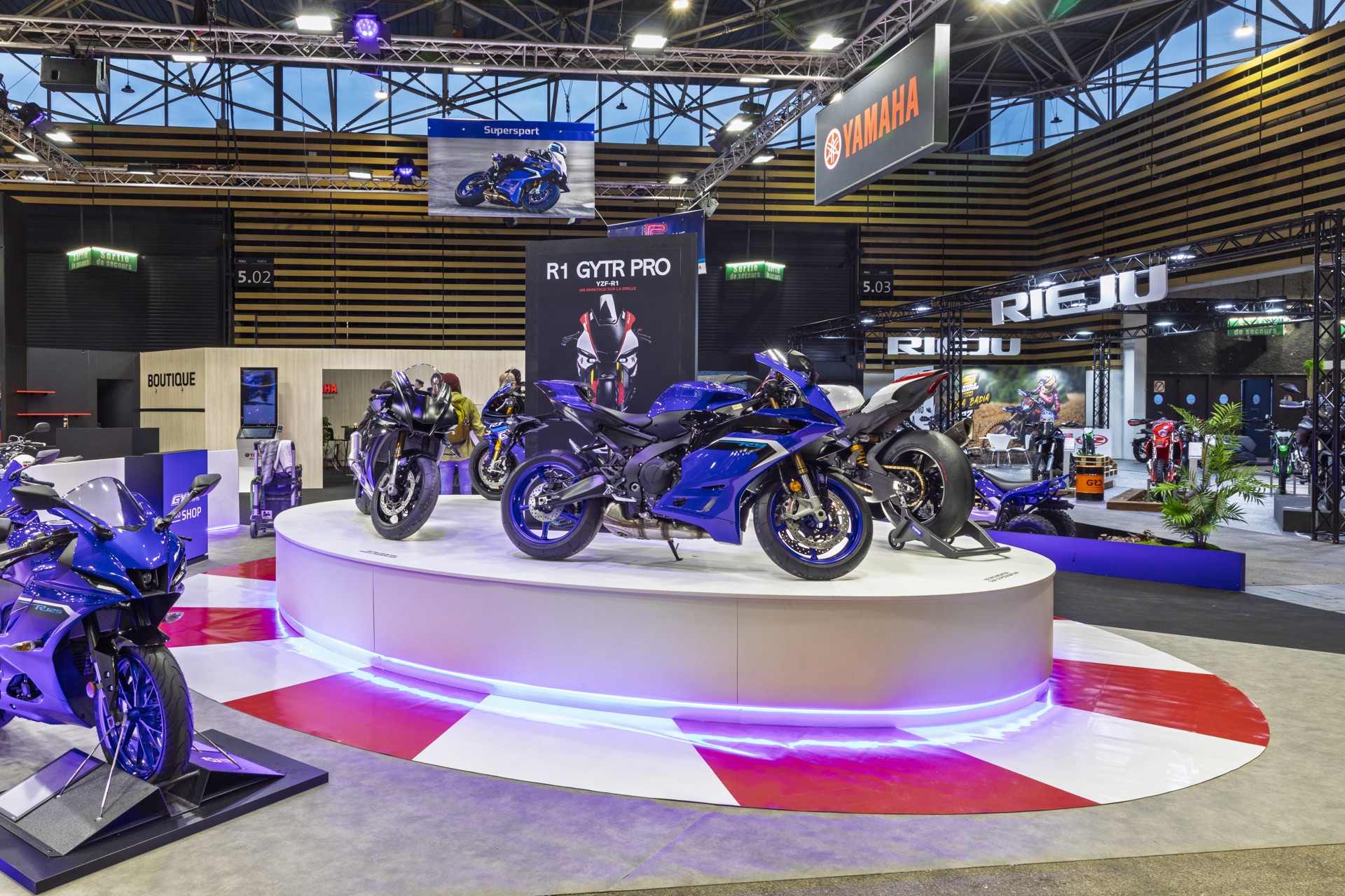 Moto Yamaha exposée sur un podium circulaire lumineux du stand, Salon du 2 Roues