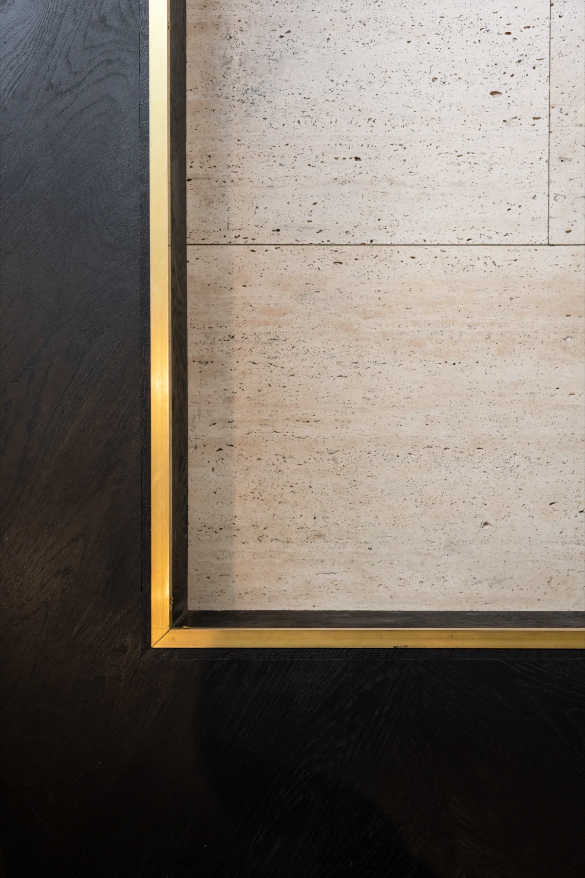 Détail d'un encadrement de laiton entre parquet de chêne teinté et pierre claire