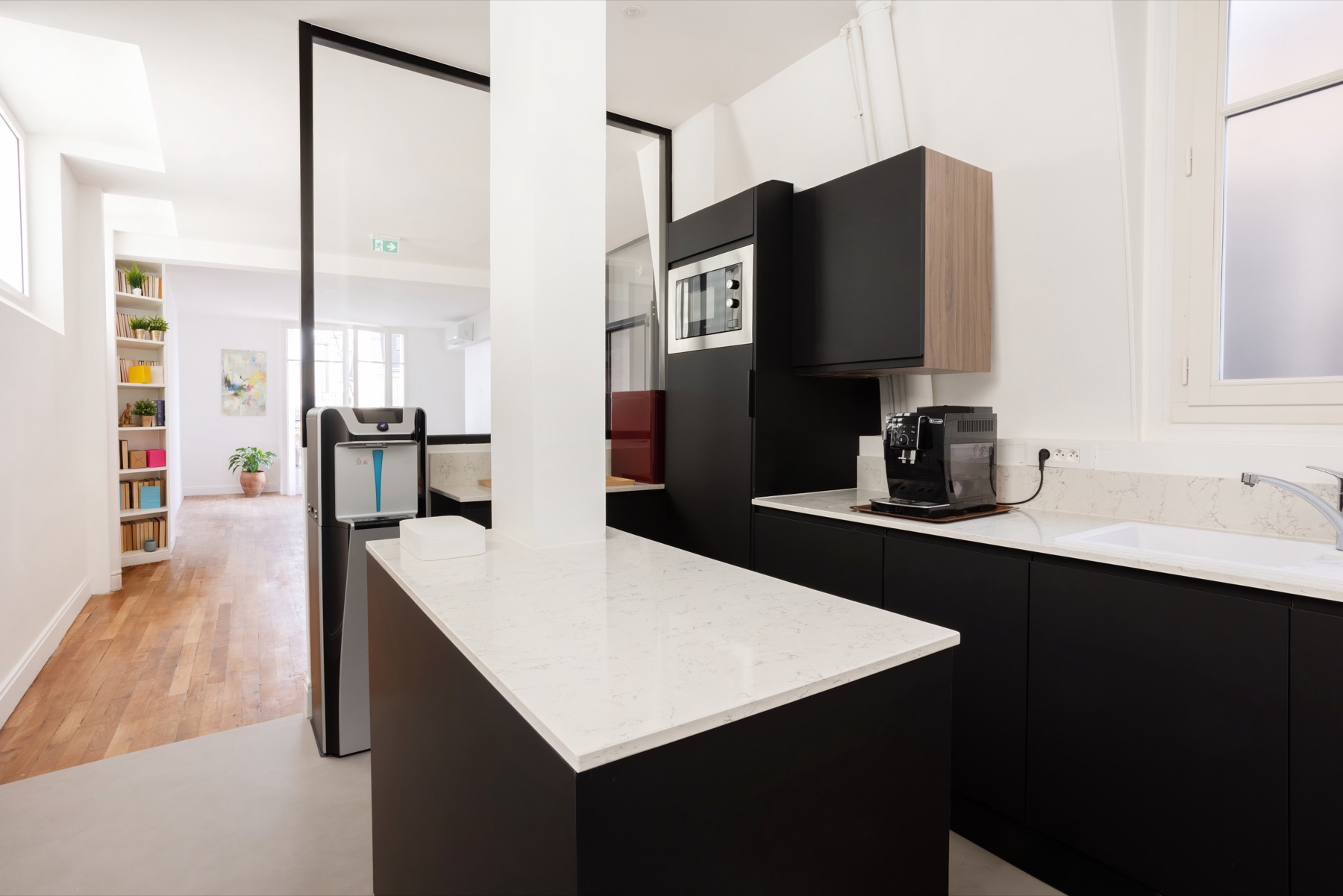 Cuisine d’équipe des bureaux Act Beauty, îlot à façades noires et plan de travail blanc veiné
