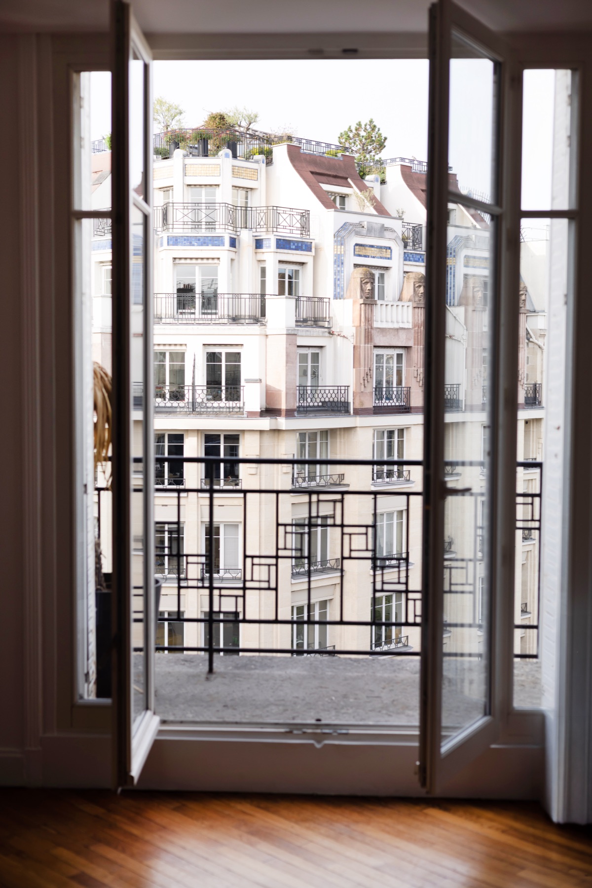 Porte-fenêtre ouverte sur un balcon en fer forgé et les façades haussmanniennes