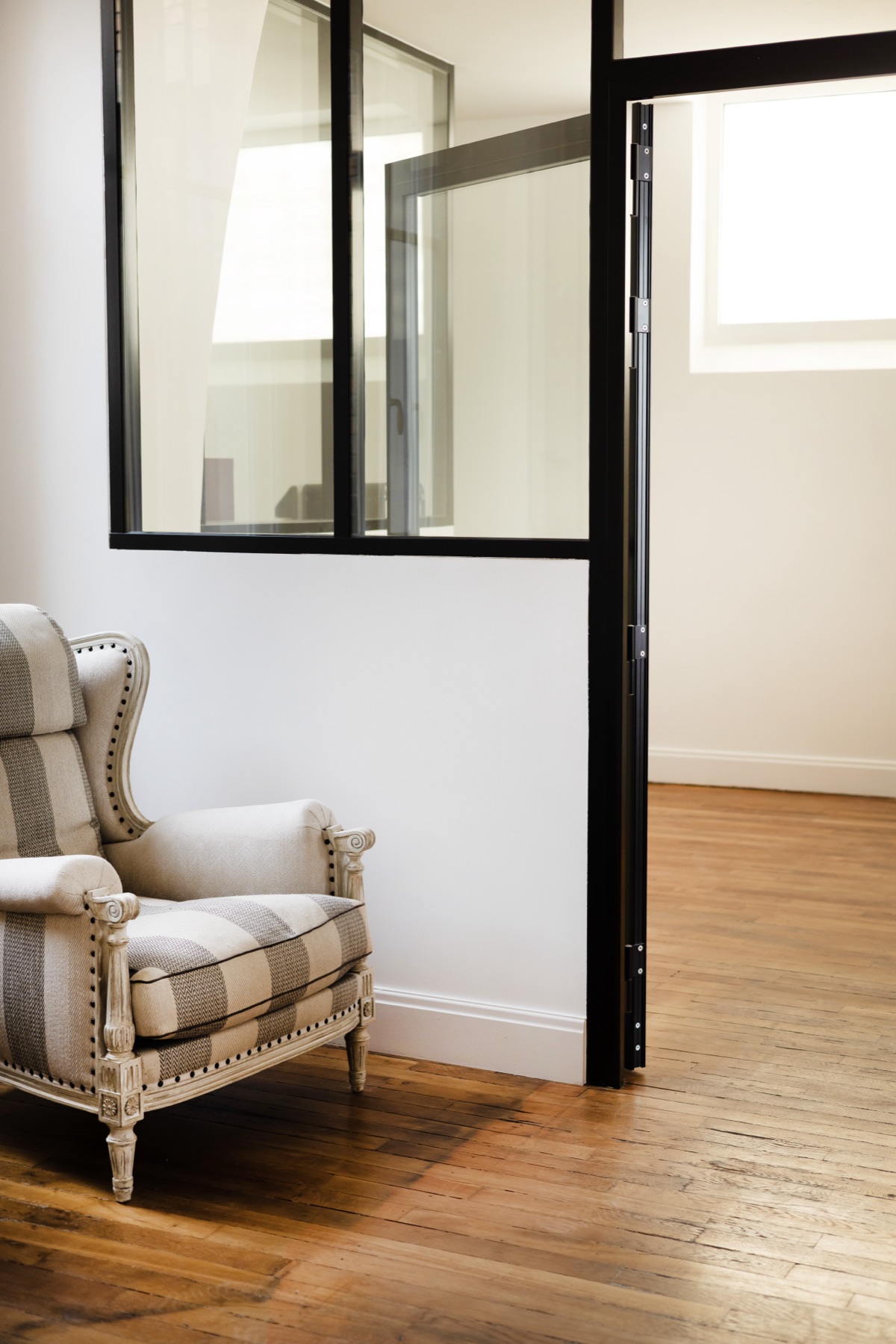 Verrière en acier noir et fauteuil à oreilles dans un bureau Act Beauty