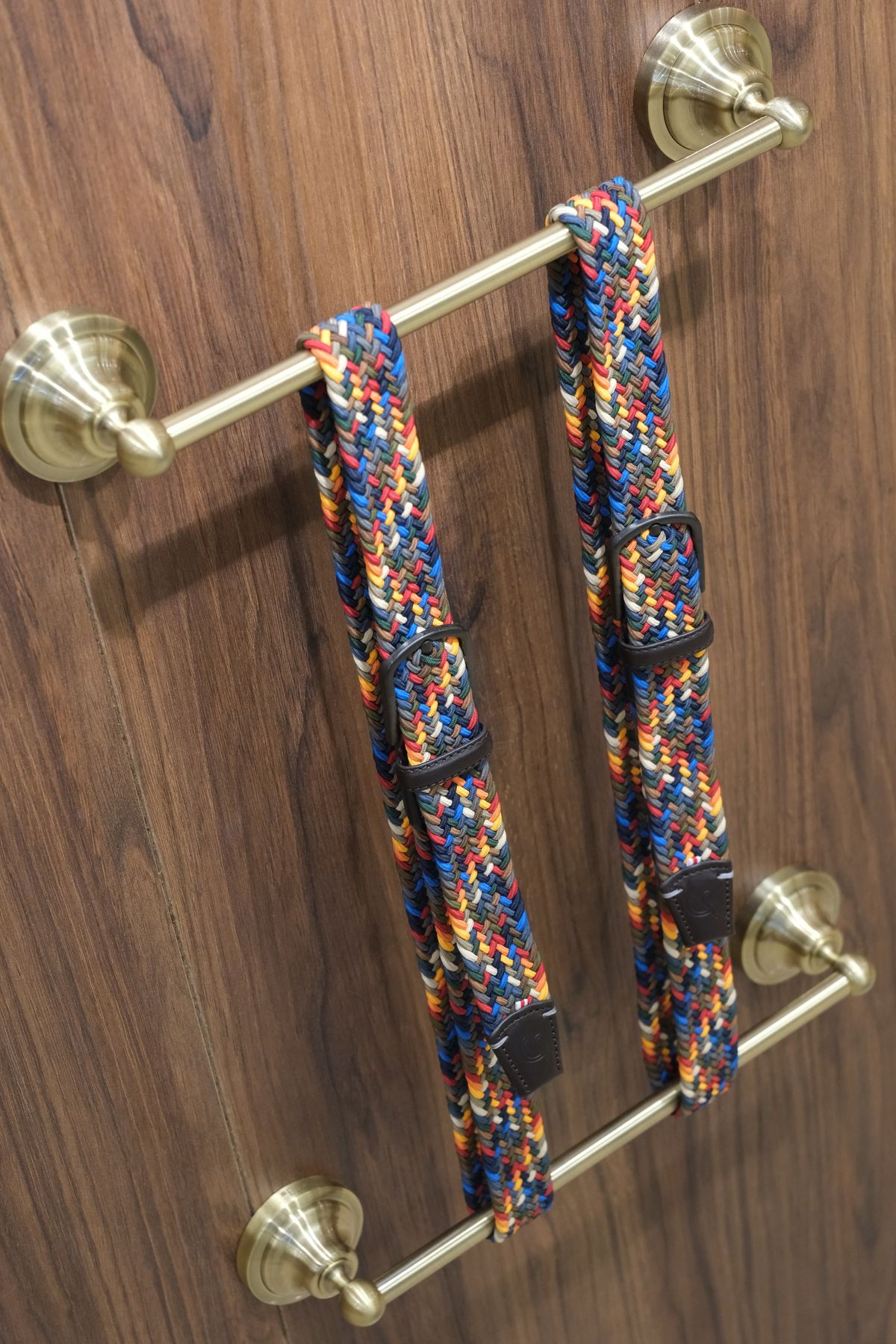 Détail de ceintures tressées multicolores sur une barre en laiton